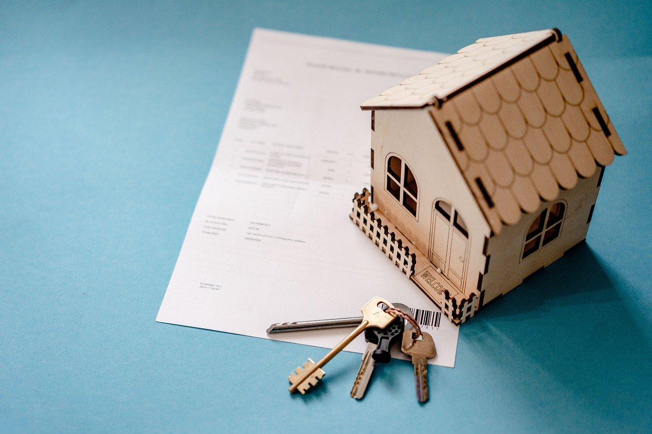 Miniature wooden house with house keys and a contract on blue surface