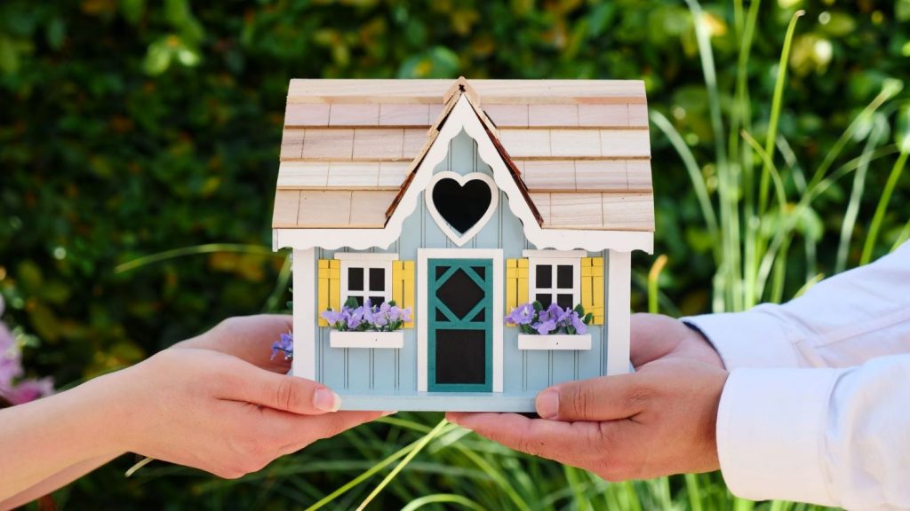 Two people holding a miniature wooden house